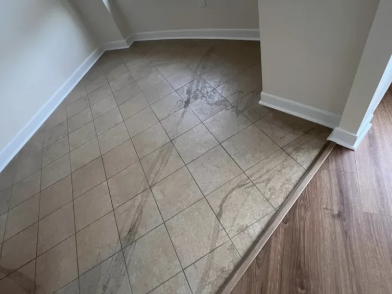 Brown tiled floor with visible dirt marks next to a wood floor in an empty room corner.