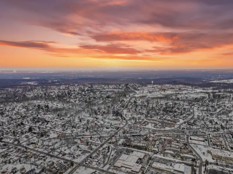 Snow-covered suburban neighborhood under a colorful sunset sky.
