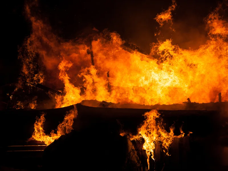 Large flames engulf a building at night with intense orange fire and dark smoke.