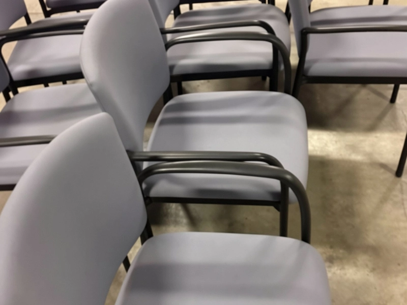 Rows of gray chairs with black metal armrests on a concrete floor.