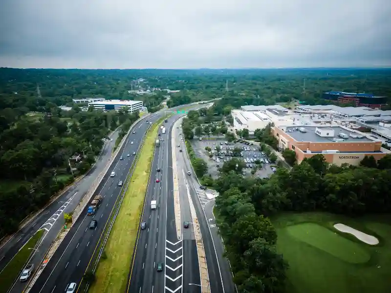 Aerial view of a highway with cars passing by next to a shopping mall and a golf course.